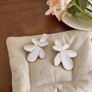 Close-up detail of white and gold flower-shaped earrings on a beige jewelry pad