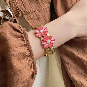 Close-up of elegant gold bangle with pink enamel daisy flowers and pearl centers on wrist