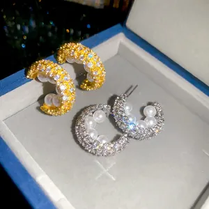 Detailaufnahme der mikropavé-gefassten Zirkonia C-Ohrringe mit eleganten weißen Perlen.
