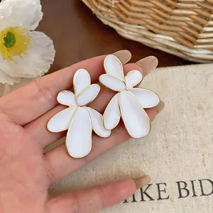 Detailed view of oversized white enamel flower stud earrings with gold trim