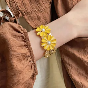Detail view of a gold-toned daisy cuff bracelet with yellow petals and pearls.
