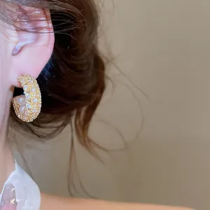 Nahaufnahme eines eleganten C-förmigen Goldohrrings mit Zirkonia-Diamanten und Perlen