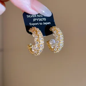 Detailansicht von eleganten goldenen C-förmigen Ohrringen mit Zirkonia und Perlen