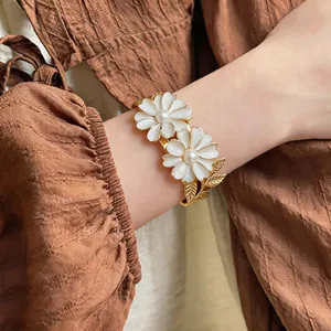 Detailed shot of an elegant gold daisy bangle featuring white enamel and pearls