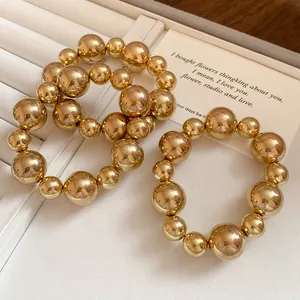 Macro detail of golden beaded bracelets set with smooth metallic finish on white tray.