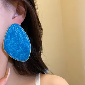 Dettaglio di un grande orecchino in smalto blu con bordo dorato indossato da una modella