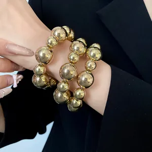 Detailed close-up of three gold smooth beaded bracelets worn on a wrist with blazer