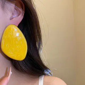 Primo piano di un orecchino geometrico irregolare giallo brillante sull'orecchio