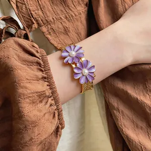 Close-up of a gold bangle featuring two elegant purple daisies with pearl centers