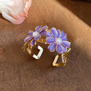 Detailed view of gold cuff bracelet with purple enamel daisies and pearl accents