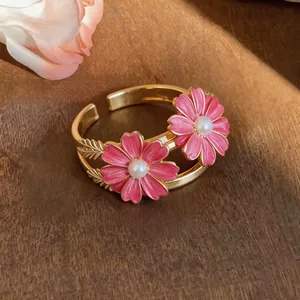 Detail of gold-toned daisy bangle with pink enamel petals and pearl center.