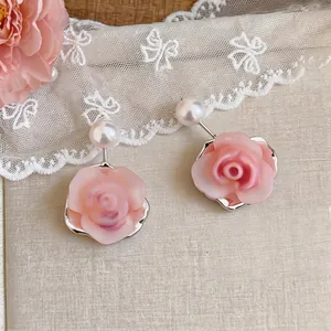 Elegant pink resin rose earrings with white pearls displayed on a soft lace background.