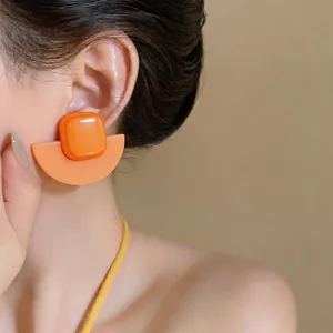 Détail de boucles d'oreilles rétro géométriques en acrylique orange portées par un mannequin