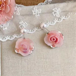 Detail view of pink resin rose and pearl stud earrings with elegant silver needles
