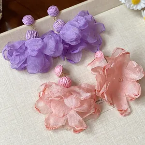 Close-up detail of romantic chiffon flower earrings with woven raffia studs for vacation