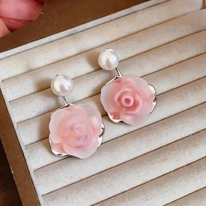 Macro detail of elegant pink resin rose earrings with pearl accent on velvet display tray