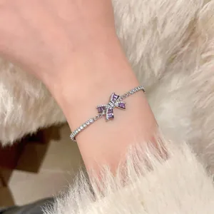 Detailed close-up of an elegant silver-tone bow bracelet featuring purple and clear zircons
