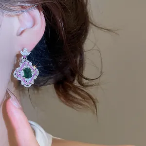 Détail de boucles d'oreilles de style cour vintage avec zircons vert émeraude et rose.