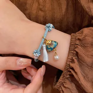 Close-up of blue hand-woven cord bracelet with landscape charm and white tassel