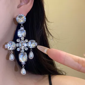 Detailaufnahme der übergroßen Kreuzohrringe mit Strass und Perlen-Tropfenanhängern