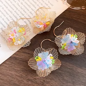 Elegante goldene Netzblumen-Ohrringe mit bunten Perlen und Perlen auf Holztisch