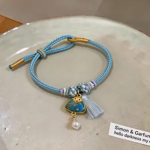 Close-up of a blue hand-woven bracelet featuring a cute triangle charm with a silk tassel.