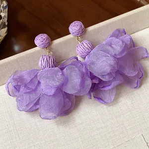 Macro detail of purple chiffon flower earrings with woven raffia balls