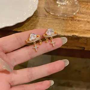 Close-up of elegant 18K gold plated planet stud earrings with a dangling crystal cross.