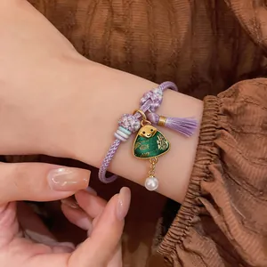 Close-up detail of a hand-woven purple rope bracelet featuring a green zongzi charm