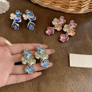 Detailed view of colorful enamel flower drop earrings held by hand on wooden background