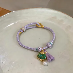 Close-up of handmade purple woven bracelet with a green triangular charm and tassel