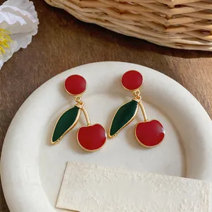 Close-up of retro red enamel cherry drop earrings with gold finish on a white tray