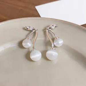 Detailed view of cherry-shaped earrings with white cat eye stones and clear zircons.