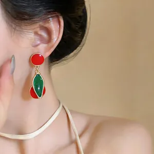 Close-up view of vintage style red and green enamel cherry pendant earrings on a model's ear