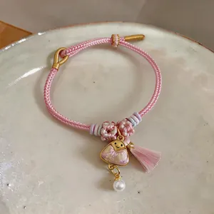 Macro view of hand-woven pink bracelet with zongzi charm, tassel, and pearl drop