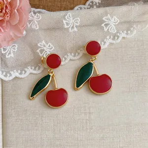 Close-up detail of vintage-style cherry drop earrings featuring red enamel and gold trim