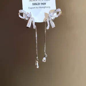 Macro detail of asymmetric bow tassel earrings featuring sparkling teardrop crystals