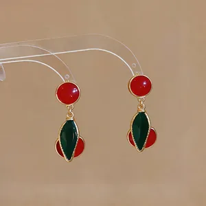 Close-up of vintage-style red and green cherry drop earrings with a glossy enamel finish.