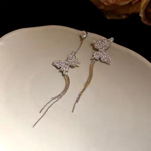 Detail view of sparkling asymmetric butterfly tassel earrings on a ceramic dish