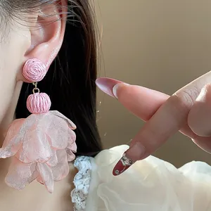 Detailed close-up showing pink raffia and chiffon flower drop earrings worn on model's ear