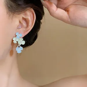 Detailed close-up of elegant blue and green enamel flower pendant earrings worn on model's ear