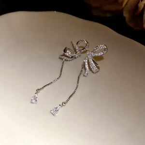 Detailed close-up of asymmetrical bow earrings with sparkling crystal tassels on a dish