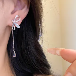 Close-up detail of asymmetrical silver bow earrings with long sparkling crystal tassels