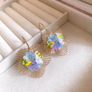 Nahaufnahme von eleganten hohlen Goldblumenohrringen mit bunten Perlenblumenmitten