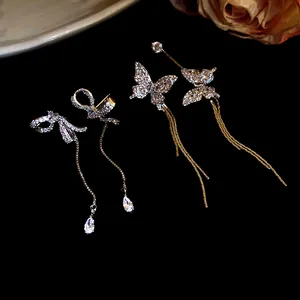 Detailed close-up of sparkling asymmetric butterfly and bow tassel earrings on black