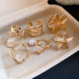 Lot de six bagues ouvertes vintage dorées avec motifs perle, fleur et étoile de mer.