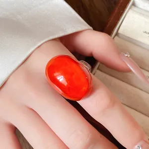 Detailed macro view of an oversized orange resin oval ring worn on index finger