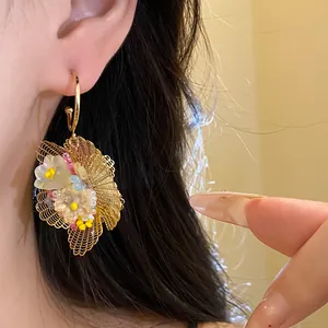 Nahaufnahme eleganter hohler Drahtgeflecht-Blumenohrringe mit bunten Perlen am Modell
