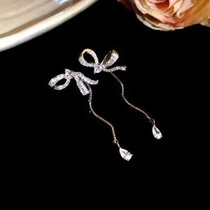 Detailed view of sparkling asymmetric bow tassel earrings with pear-shaped drops on black