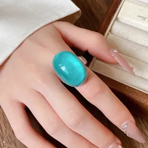 Detailed view of a large turquoise oval resin ring worn on a finger for showcase.